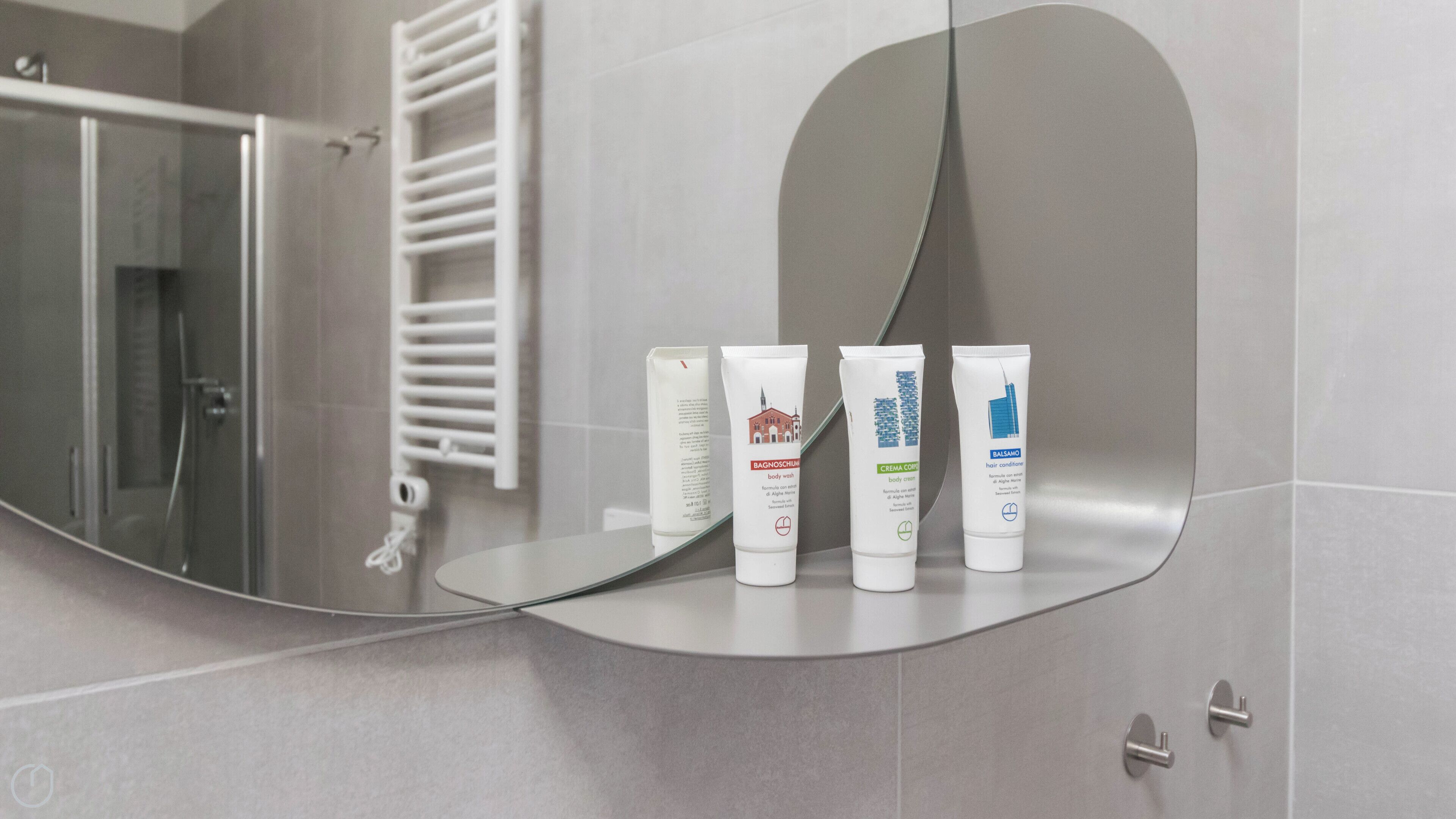 A bathroom with a large mirror reflecting a shower area and a towel rack. Three toiletries are visible on the mirror's surface.