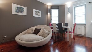 Uma sala de estar moderna com um sofá redondo, uma mesa de jantar com cadeiras e duas obras de arte emolduradas na parede.