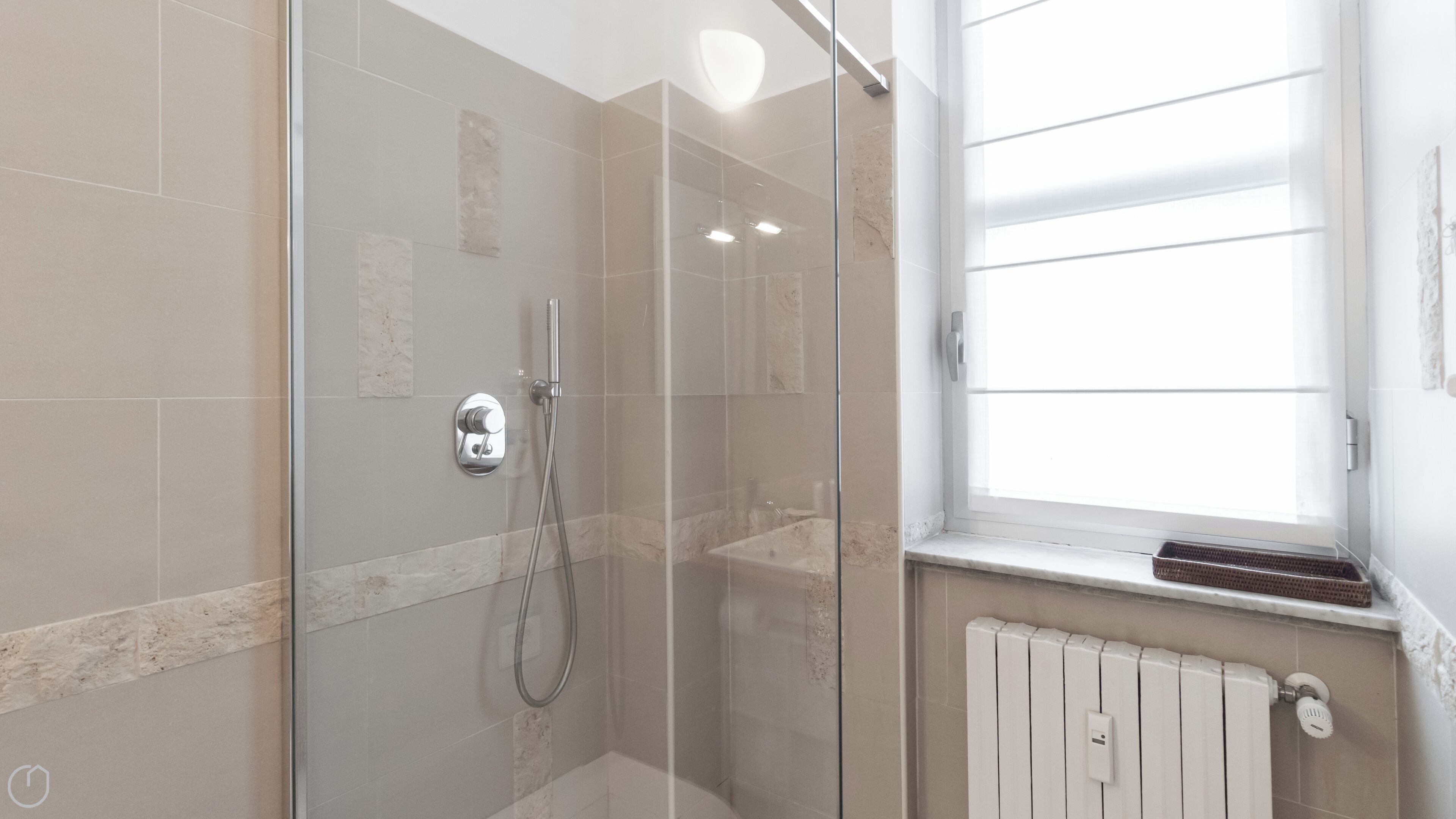 Ein modernes Badezimmer mit Duschkabine aus Glas, einem weißen Heizkörper und einem Fenster mit Jalousien.