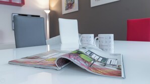 Quarto de hotel com uma mesa branca, uma revista, duas canecas brancas com a marca Italianway e uma cadeira vermelha.