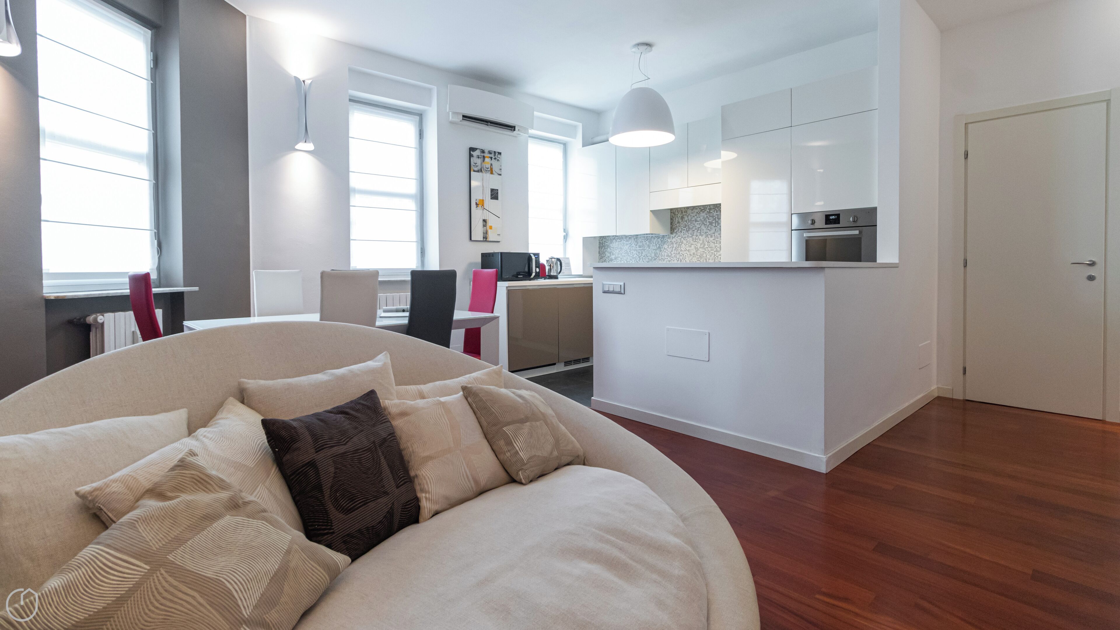 A modern living room with a large sofa, a dining area, and a kitchen with white cabinets and a countertop.