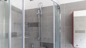 A modern shower enclosure with a glass door, a handheld showerhead, and a wall-mounted faucet.