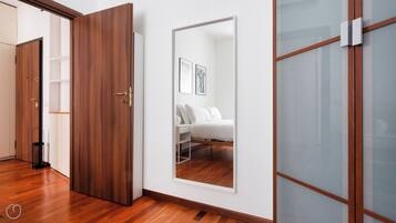 A room with a wooden wardrobe, a bed with white bedding, and a large mirror on the wall.