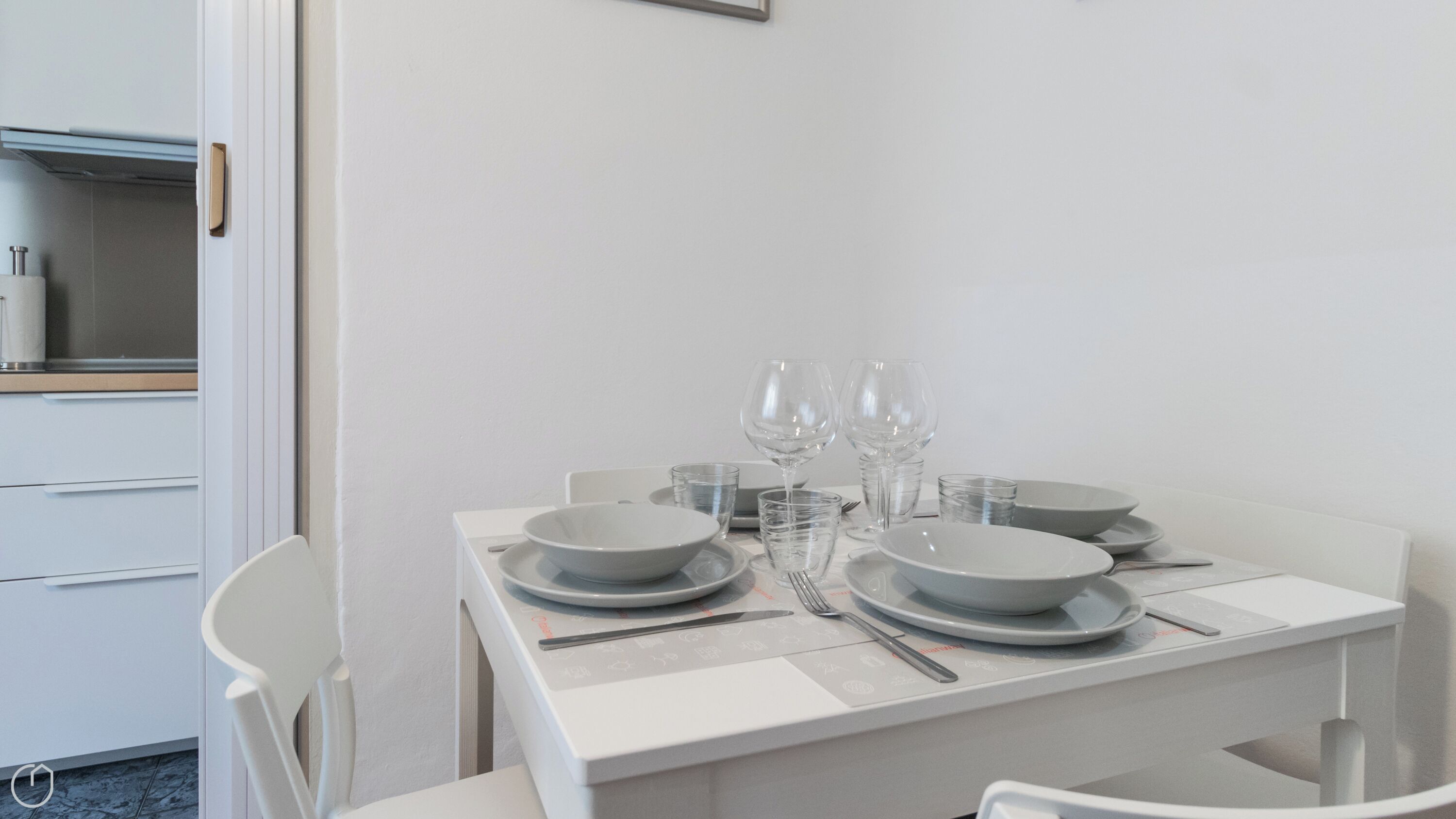 Une table à manger dressée avec des assiettes, des verres et des couverts, avec un buffet blanc et des chaises en arrière-plan.