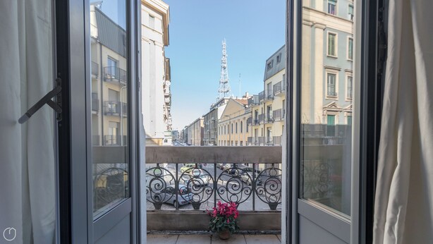 A balcony with a metal railing, a potted plant, and a view of a cityscape with buildings and a tower. - Italianway - Dei Transiti 7 (Milan)