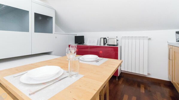 Eine moderne Küche mit weißen Schränken, einem Holztisch gedeckt mit Tellern und Besteck, einem Wasserkocher und einem Toaster.