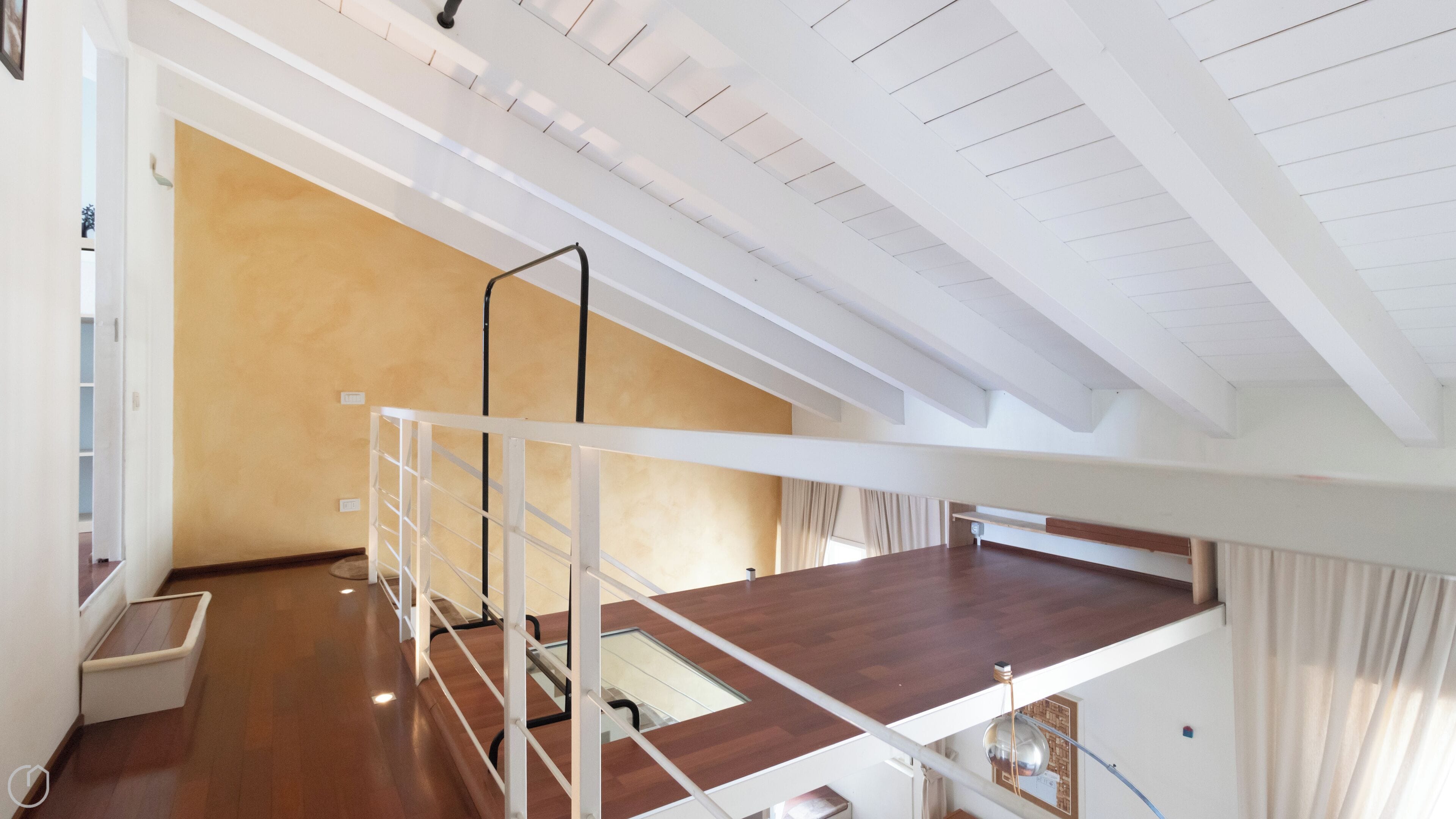 A high-ceilinged room with a wooden floor, a white railing, and a view of a lower level.