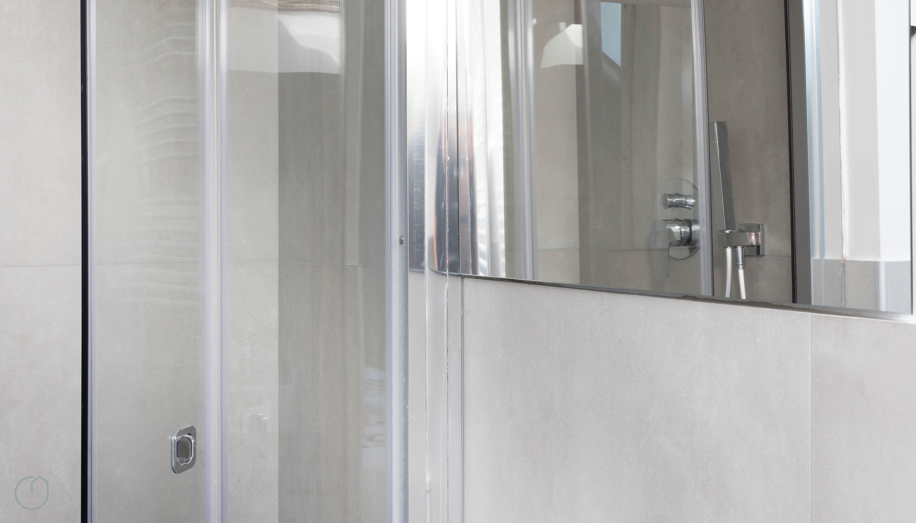 Baño con cabina de ducha de vidrio, ducha visible y grifo metálico.