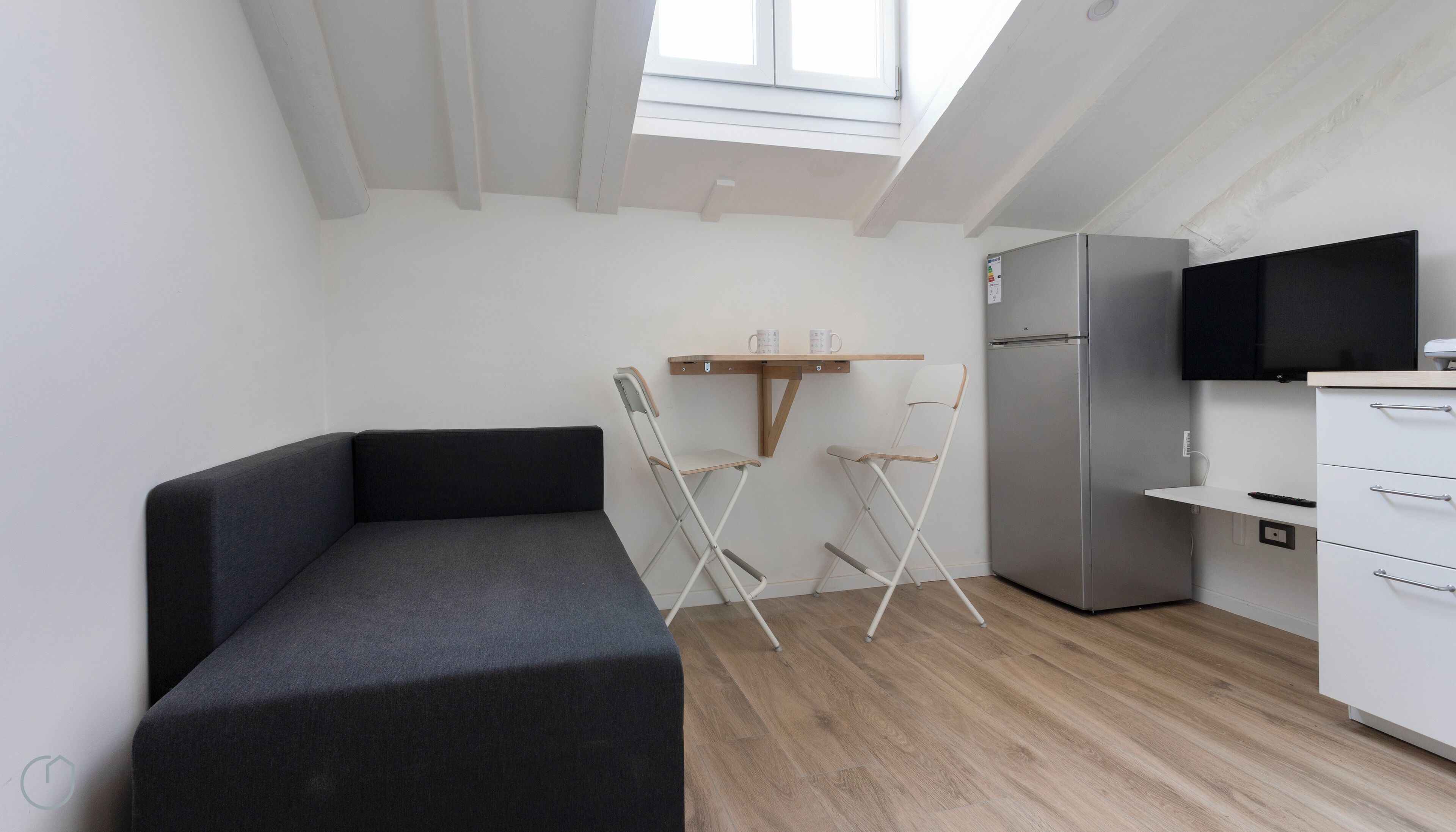 Une petite cuisine équipée comprenant un réfrigérateur intégré, un téléviseur à écran plat et une chaise pliante.