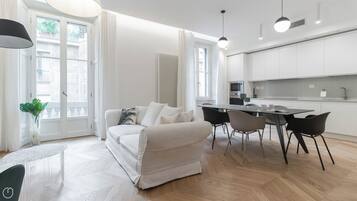 A modern living room with a sofa, dining table, chairs, and a kitchen area with cabinets and appliances.