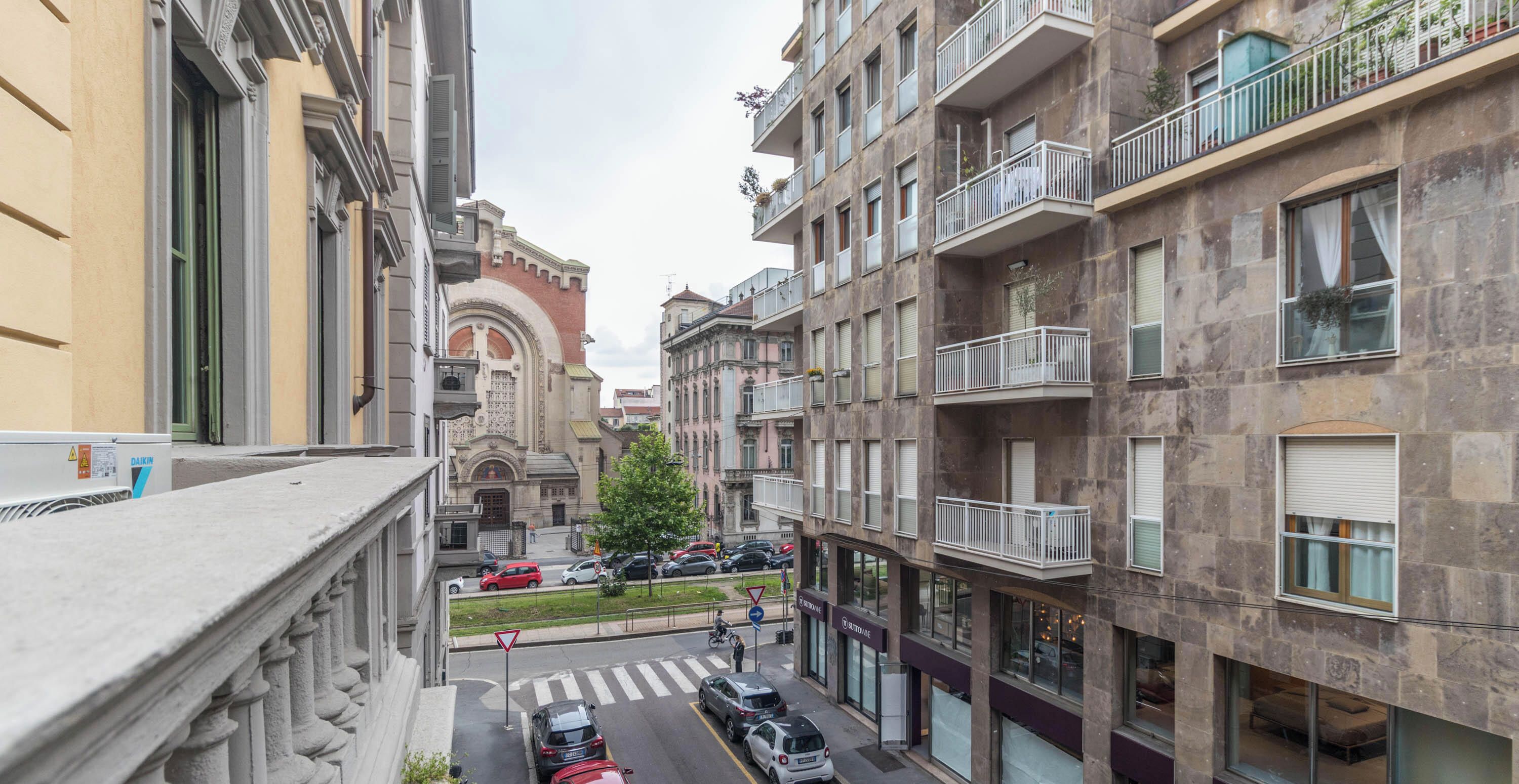 A multi-story urban building with balconies, a street view, and parked cars.