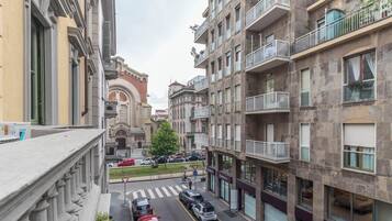 A multi-story urban building with balconies, a street view, and parked cars.