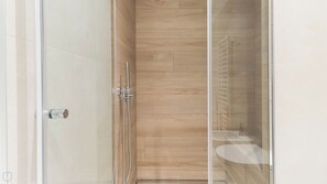 A modern shower with a glass door, a wooden panel wall, and a visible toilet in the adjacent room. - Italianway - Pindemonte 1 (Milan)