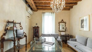 A living room with a glass dining table, a grey sofa, a wooden TV stand, and a chandelier. - Italianway Easy - Ripa Ticinese 53 B (Milan)