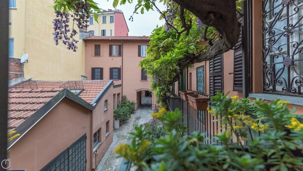 A narrow alleyway between buildings with a tiled roof, a wrought iron gate, and a small garden area with potted plants. - Italianway Easy - Ripa Ticinese 53 B (Milan)
