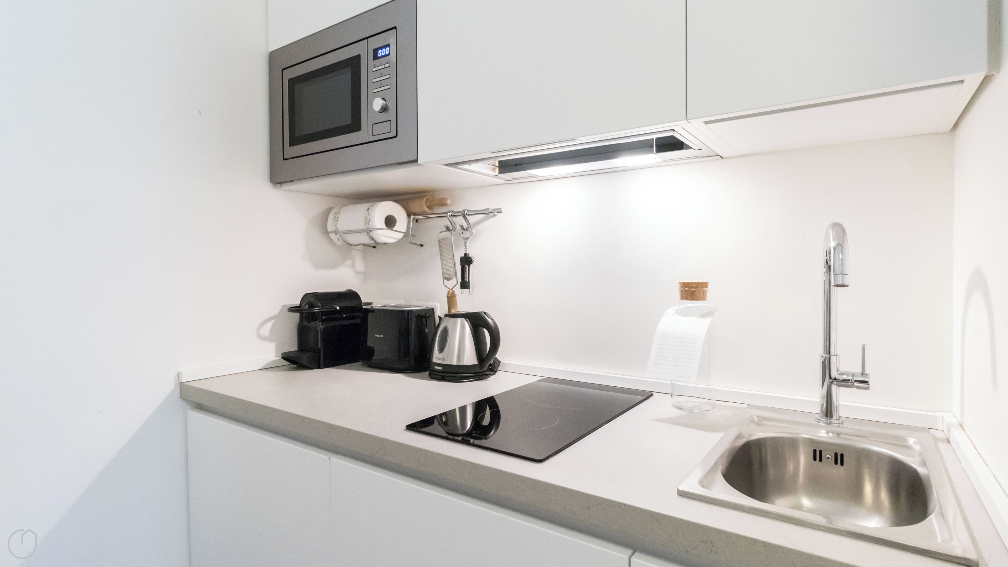 A compact kitchenette with a microwave, coffee maker, kettle, and a stainless steel sink.