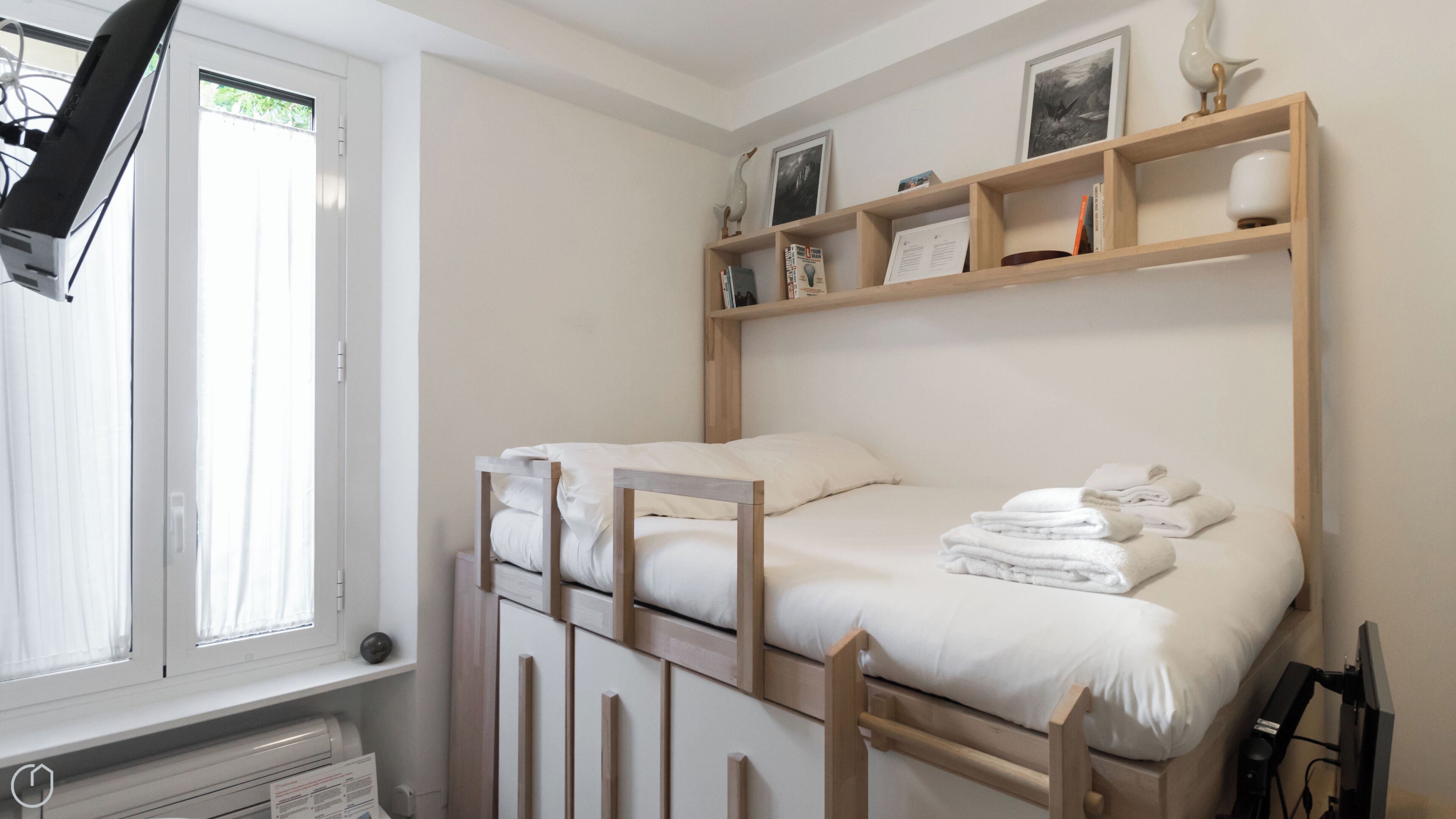 Een slaapkamer met twee bedden, een raam en een plank met boeken en decoratieve objecten.