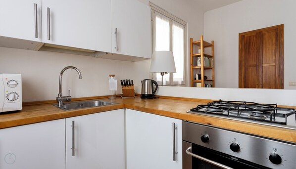 Una cocina moderna con armarios blancos, electrodomésticos de acero inoxidable, una estufa a gas y un ventanal con cortinas.