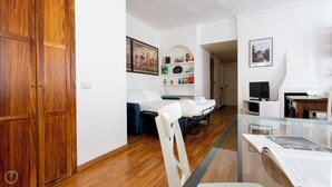 Et moderne hotelværelse med et træskab, en seng med hvide sengetøj, en blå sofa, et lille bord med et fjernsyn og en reol med forskellige genstande.