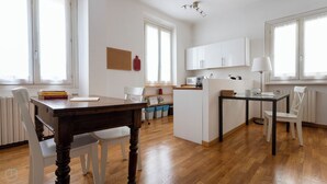 Et moderne køkken med hvide skabe, et spisebord og stole. Der er en lille ø med en vask og en mikrobølgeovn.