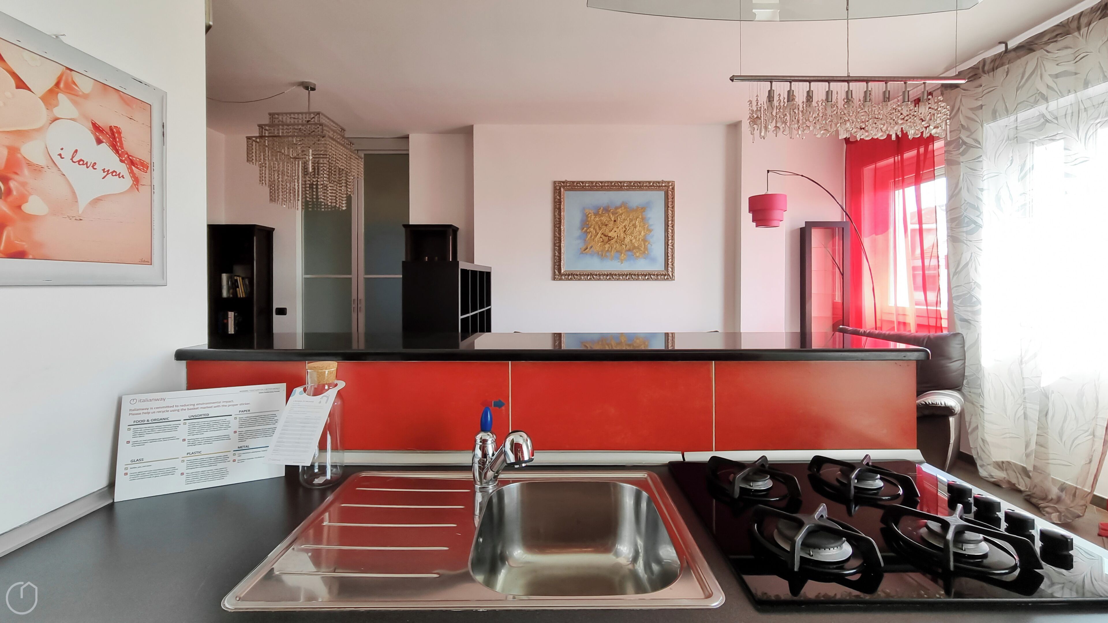 A modern kitchen with a red countertop, stainless steel sink, and gas stove.