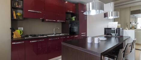 A modern kitchen with red cabinets, a central island, stainless steel appliances, and a dining area with chairs.