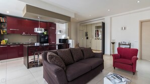 A modern living room with a dark brown sofa, a red armchair, and a kitchen area with red cabinets and stainless steel appliances. - Italianway Easy - Dall'ongaro 24 (Milan)