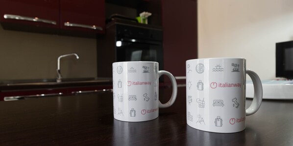 Two white mugs with Italianway logos and travel-related icons on a kitchen counter. - Italianway Easy - Dall'ongaro 24 (Milan)