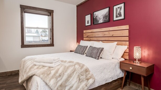 Une chambre à coucher avec une tête de lit en bois, un grand lit recouvert d’une couette blanche, un plaid moelleux et une table de chevet avec une lampe.