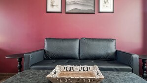 Une pièce comprenant un canapé en cuir noir, un plateau en bois orné de sculptures et trois œuvres d’art encadrées accrochées au mur.