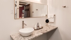 Une salle de bain avec un grand miroir, un lavabo blanc, un plan de toilette en marbre et un porte-serviettes.