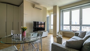 Un soggiorno moderno con un tavolo da pranzo in vetro, un divano, una TV e un'ampia finestra con vista sulla città.