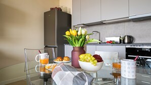 Una cucina moderna con un tavolo in vetro apparecchiato per la colazione, con croissant, frutta e un vaso di tulipani.