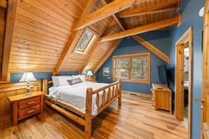 Een slaapkamer met een houten plafond, een bed, een nachtkastje, een lamp, een raam en een televisietoestel.