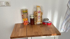 Een klein houten tafeltje met een witte lade, een prullenbak en verschillende etenswaren erop.