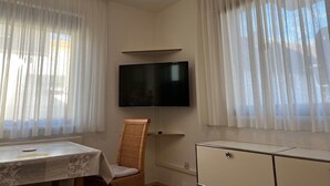 Een kamer met een aan de muur bevestigde televisie, een rieten stoel, een klein tafeltje en een kast.