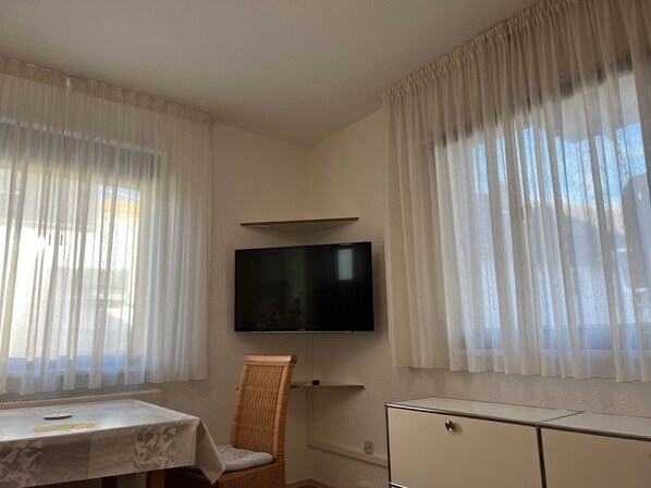 A room with a television mounted on the wall, a wicker chair, a small table, and a cabinet.