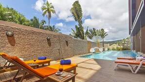 Uma área à beira da piscina com espreguiçadeiras, uma mesa com uma taça de vinho e um muro de pedra.