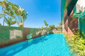 A swimming pool with clear blue water, surrounded by a brick wall and palm trees. - Chic Condo apartment by Lofty (Karon)