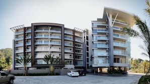 Um hotel moderno de vários andares com fachada curva, varandas e área de estacionamento.