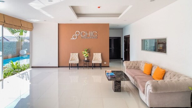 Um lobby moderno com uma mesa de recepção, duas poltronas, um sofá e uma mesa de centro. Uma grande placa diz "CHIC CONDOMINIUM".