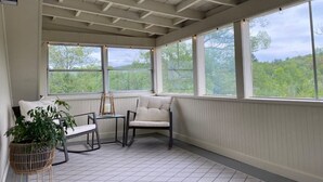 A covered porch with a view of greenery, a white chair, a small table, and a potted plant. - Top Floor River View Apartment (Kingfield)