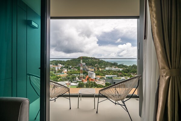 A balcony with two chairs and a table, overlooking a coastal town with buildings and greenery.