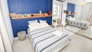 A bedroom with a bed, a chair, a shelf with decorative items, and a mirror. - Magnifique Design T2, Confortable, Parking Gratuit (Nice)