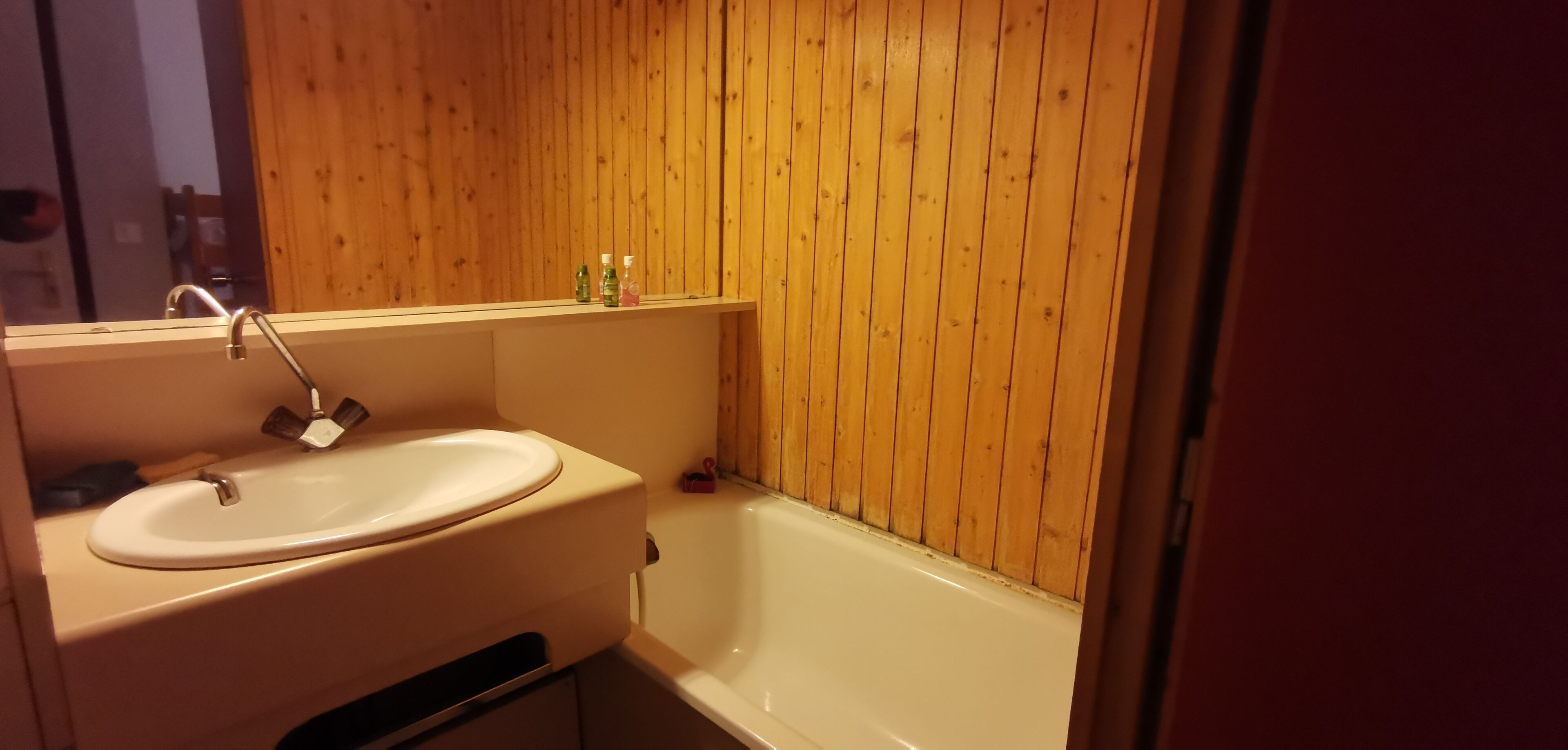 A bathroom with a wooden wall, a sink, and a bathtub.