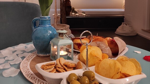 Ein Esstisch mit Snacks, eine Vase mit einer Rose und eine Kerze in einem Raum mit einer Steinwand und einem Bett im Hintergrund.