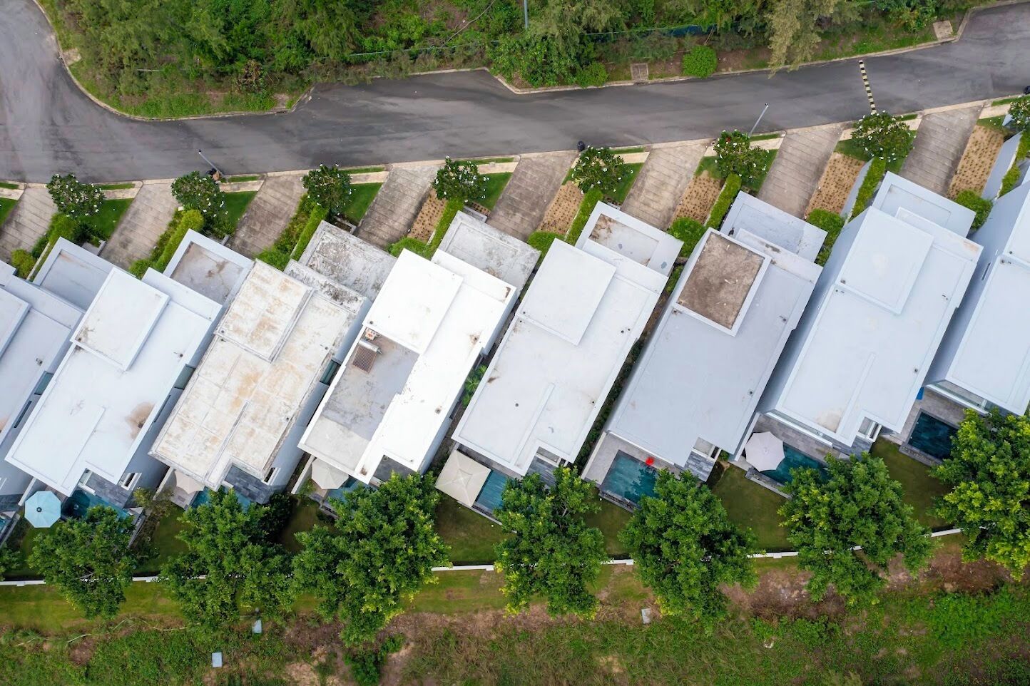 An aerial view of a row of industrial-style buildings with flat roofs, arranged in a linear fashion along a road.