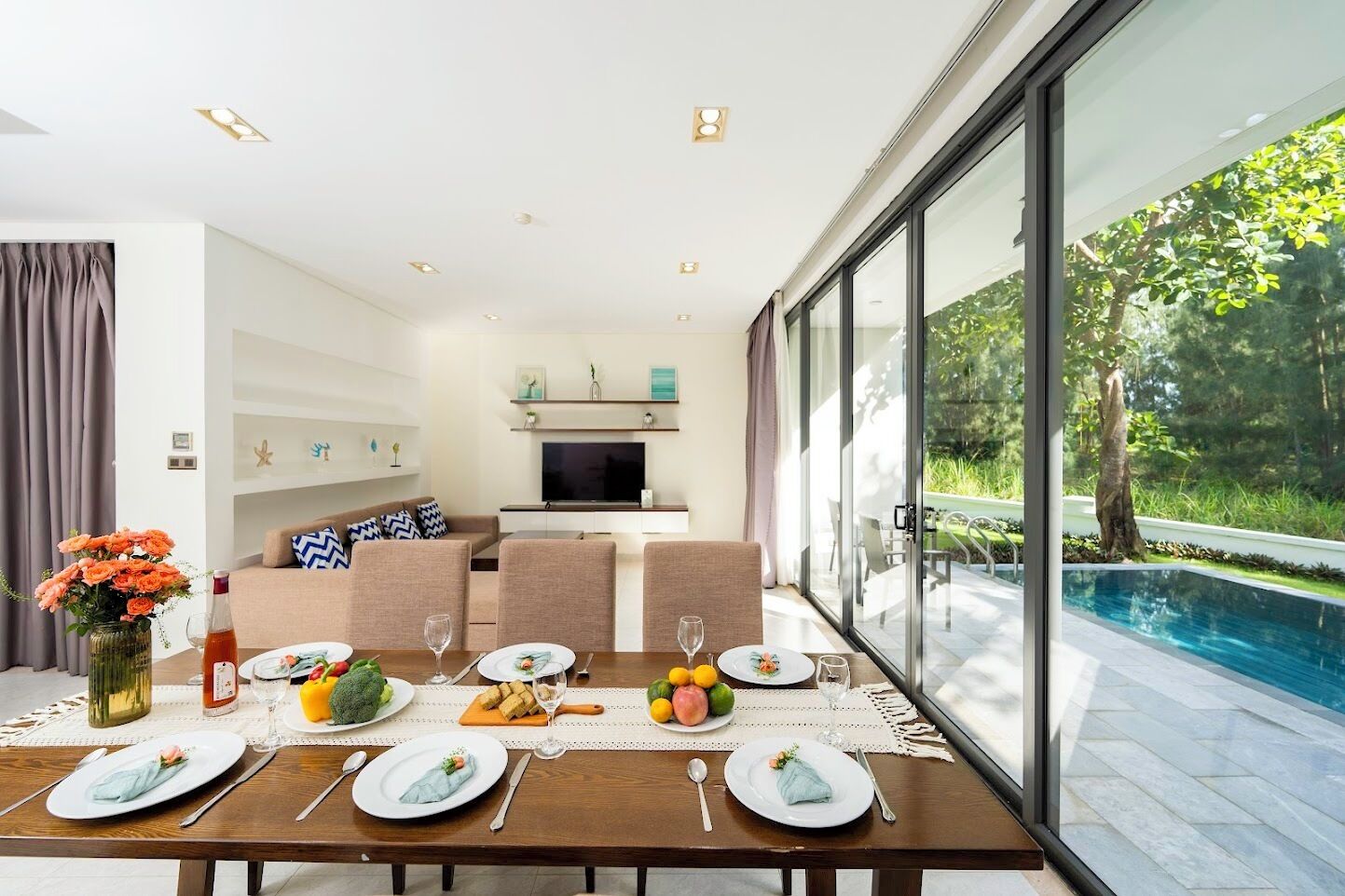 A modern dining area with a table set for four, a sofa, and a TV in the background.