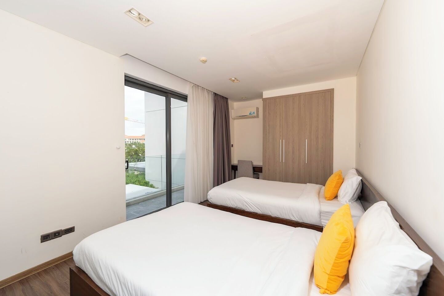 A modern hotel room with two beds, a large window, and a wardrobe.