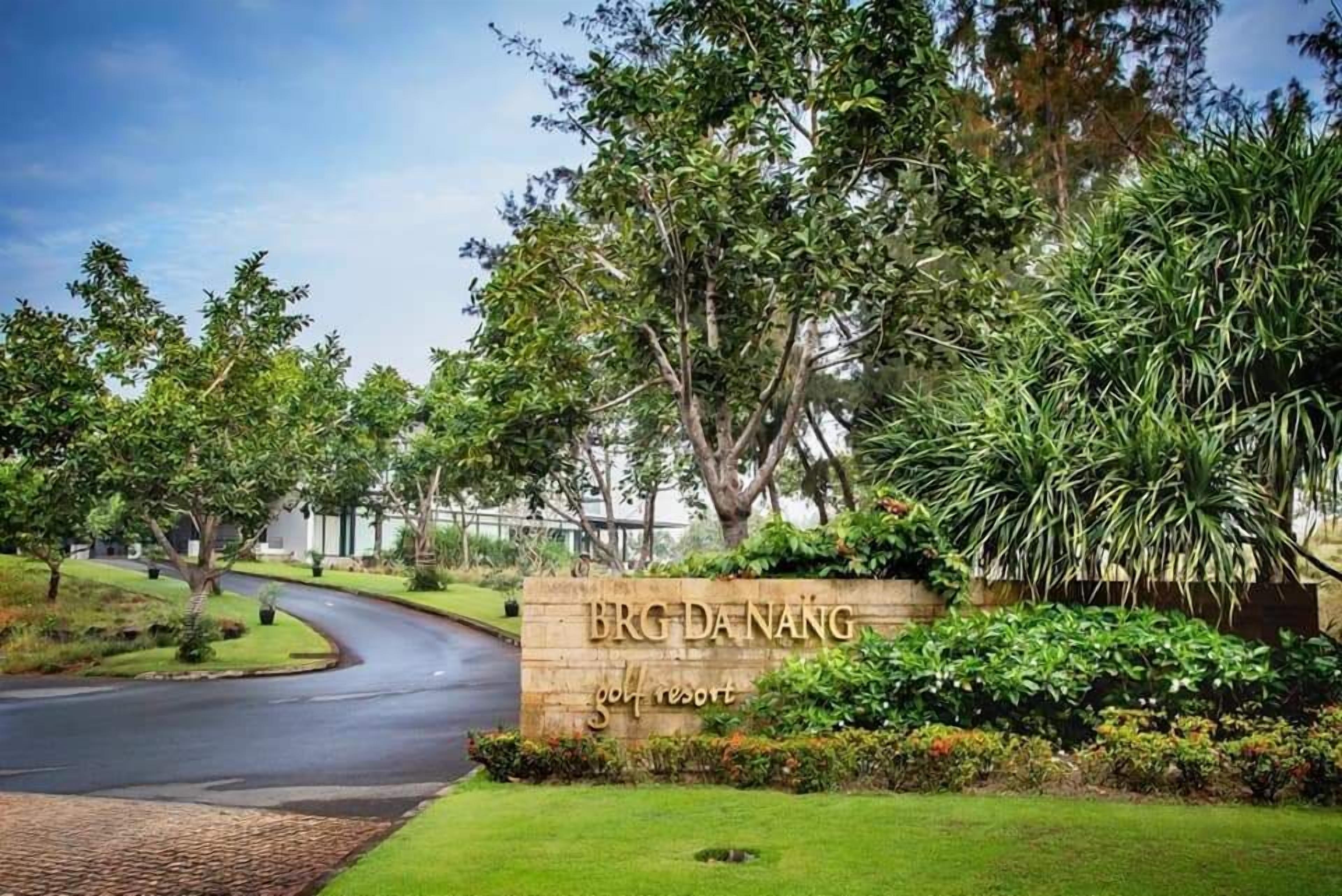 A golf resort entrance with a curved driveway, lush greenery, and a sign that reads "BRG DA NANG golf resort."